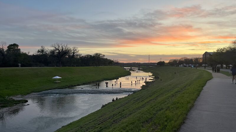 The Clear Fork of the Trinity at dusk: the paved trail running along the bank, anglers standing out in the shallows, sunset over the bridge.